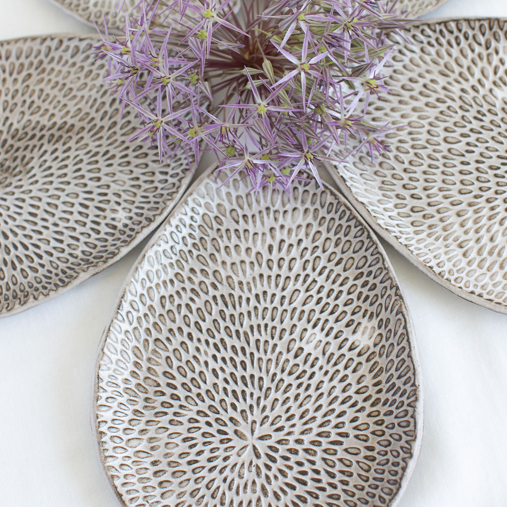 Five Petal Palette appetizer plates arranged like petals around a purple flower, highlighting White Matte glaze over dark clay.