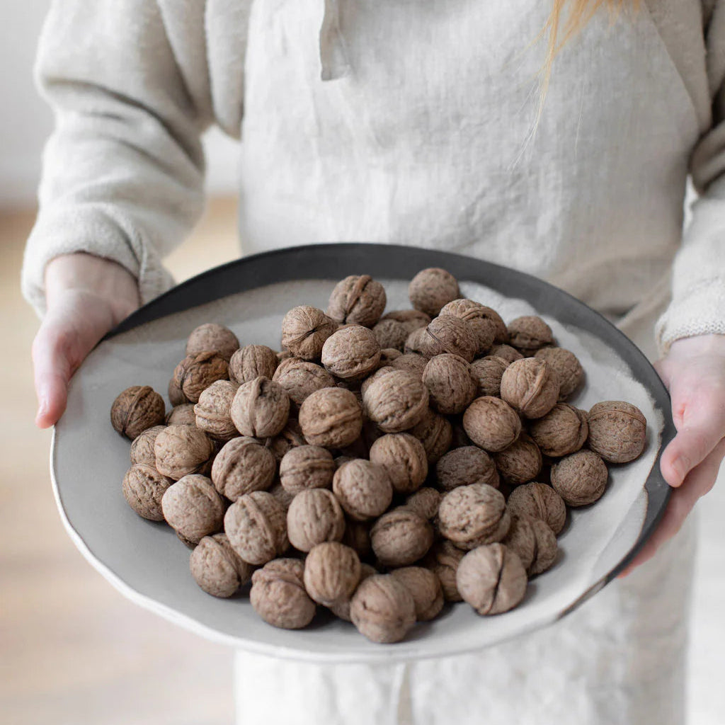 Person in a linen apron holding a walnut-filled Rustic Pour Over round serving bowl, showing its size and shallow profile.
