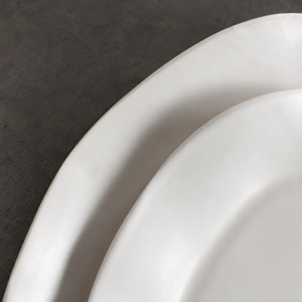 Close-up of overlapping White Matte platter rims showing their softly irregular edges and glazed surfaces.
