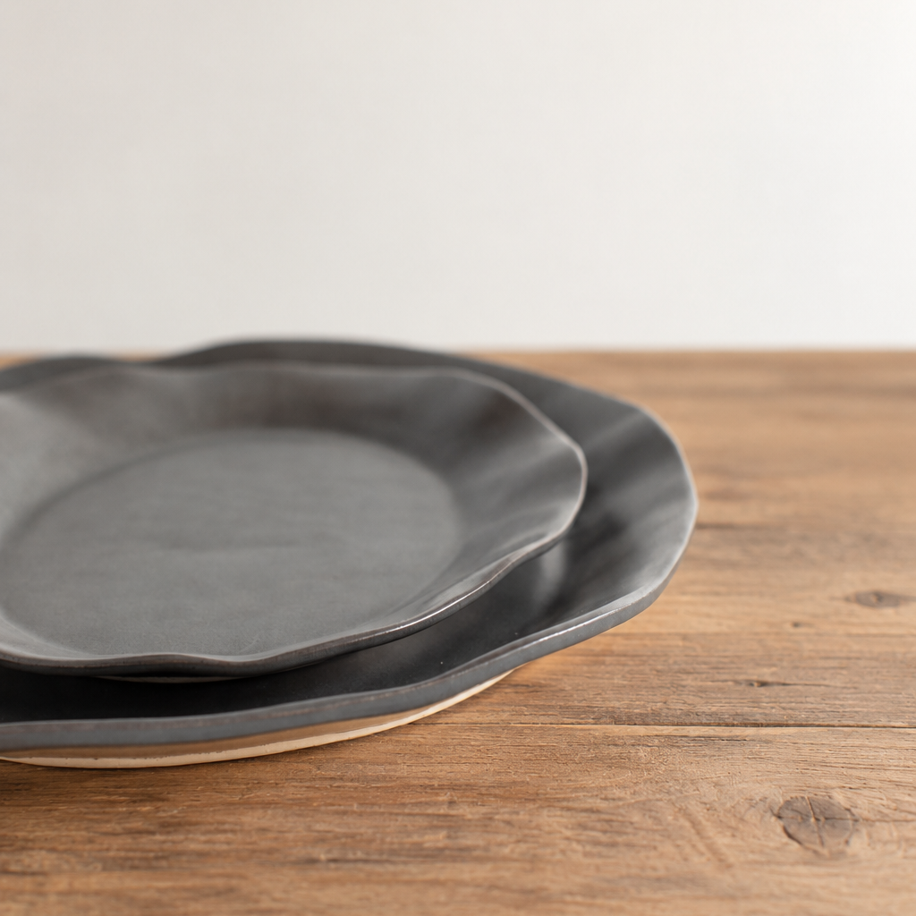 Two nested Charcoal Shino oval stoneware platters on a rustic wooden table, showing their shallow profiles and softly irregular rims.