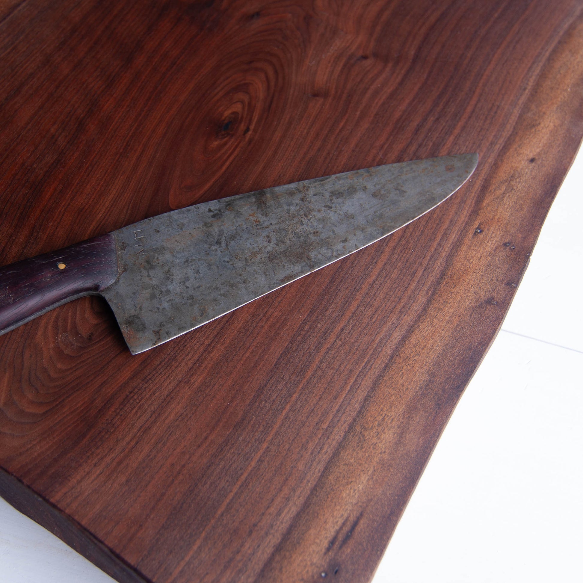 A close up of a walnut cutting board to show the figured grain with a kitchen knife on top