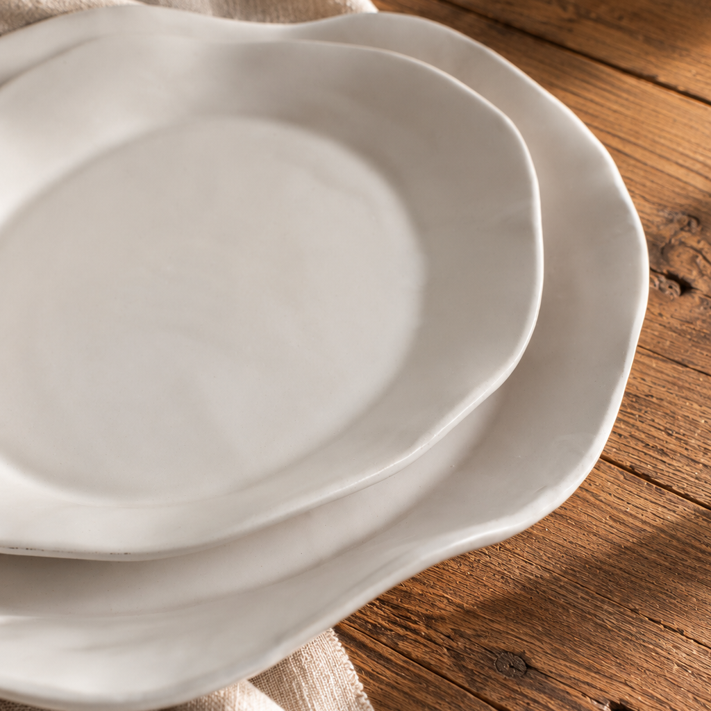 Angled close-up of two stacked White Matte oval serving platters on a rustic wooden table, showing their gently curved rims.