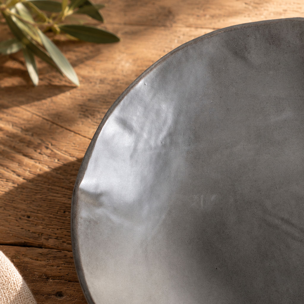 Close-up of a Charcoal Shino serving bowl showing its softly irregular rim and varied gray glaze on a wooden table.