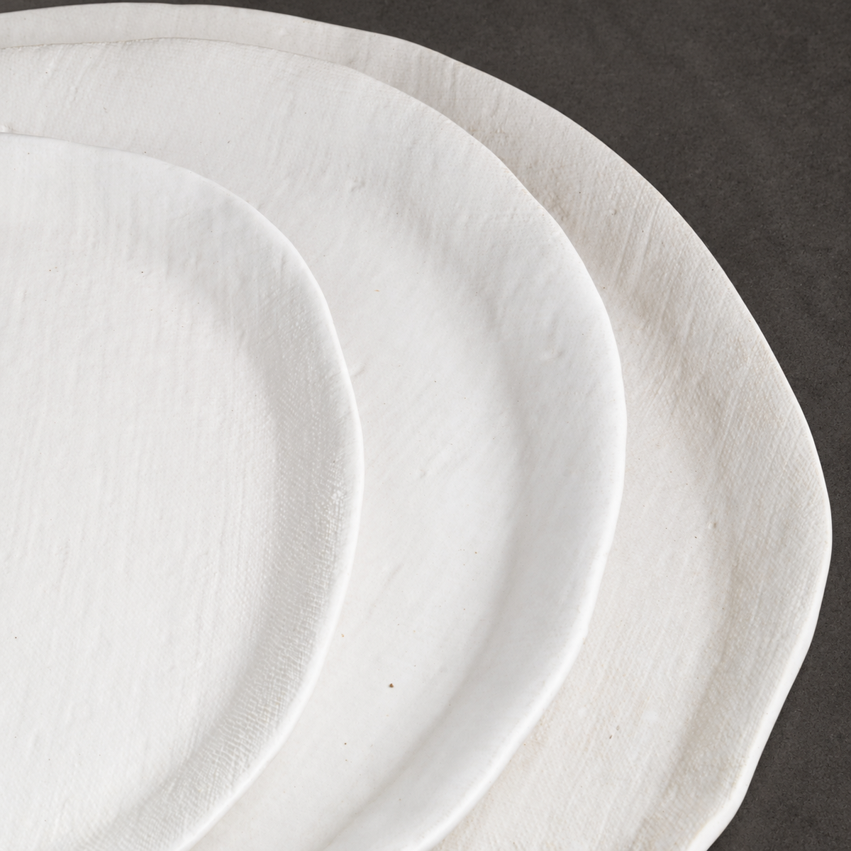 Close-up of overlapping White Matte oval platters showing their linen-textured surfaces and curved edges.