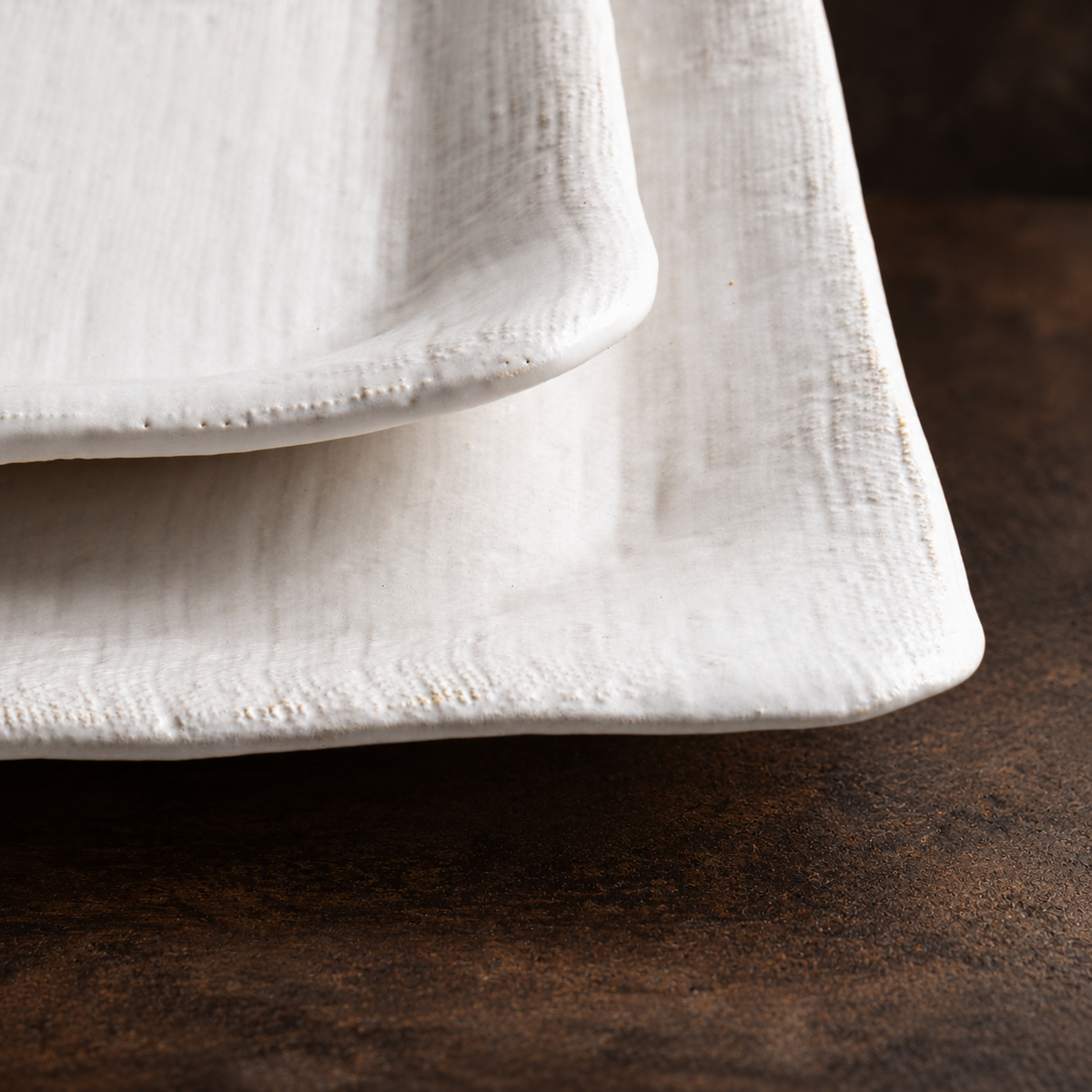 Close-up of overlapping White Matte platters showing linen texture, raised rims, and softly irregular edges.