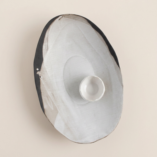 Rustic Pour Over oval serving bowl with a small white bowl inside, on a square pale background.