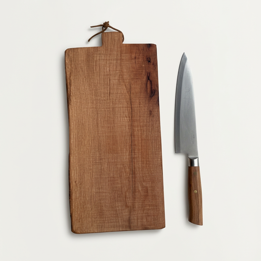 Number 228 Oregon White Oak serving board with a leather hanging loop, styled beside a knife on a porcelain-white background.
