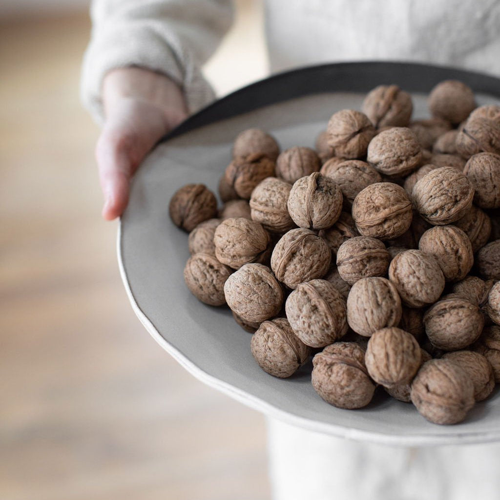 Close-up of a person holding a Rustic Pour Over round serving bowl filled with whole walnuts, showing its white glaze and dark rim.